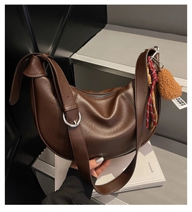 Detail of dark brown crescent shoulder bag with leather texture and teddy bear charm