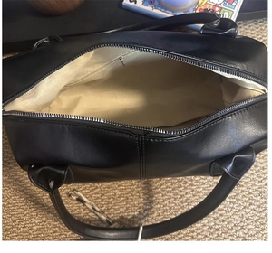 Detail view of the spacious interior with beige lining and zipper pocket of a black bag