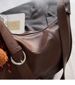 Detailed close-up of dark brown leather shoulder bag with metallic zipper and pompom