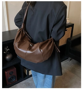 Detail of large dark brown leather crescent bag with stylish pleated texture worn by model