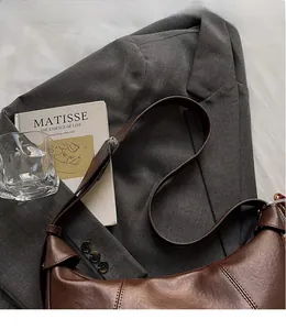 Detail of a brown leather shoulder bag featuring a smooth long strap and crescent design
