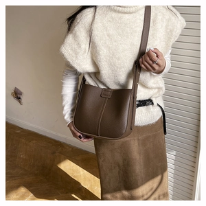 Deep brown pebble leather crossbody bag shown on a model in a sunlit indoor setting