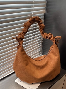 Brown faux suede crescent tote bag with scrunchie handle and bow detail under window light