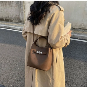 Detail of dark brown lychee leather bucket bag with silver twist lock on beige trench coat