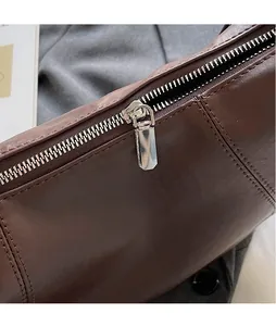 Close-up of smooth silver metal zipper and fine stitching on brown leather shoulder bag