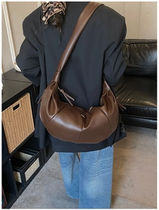 Detail of dark brown leather pleated crescent bag worn by a model in a minimalist room