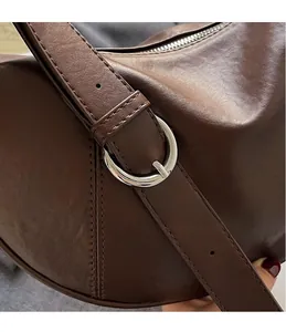 Detail of silver circular buckle and fine stitching on dark brown crescent leather bag