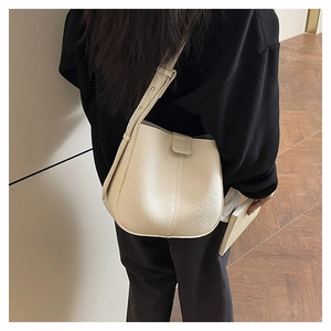 Detail of creamy litchi grain leather bucket bag with adjustable shoulder strap on model