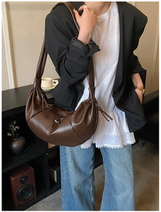 Detail of a brown pleated crescent bag featuring textured faux leather and strap details