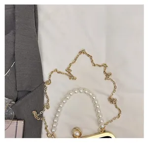 Detail of elegant top handle bag featuring luxury white pearl beads and gold chain strap