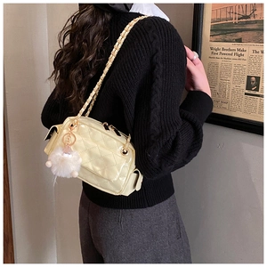 Détail d'un sac bandoulière beige matelassé avec chaîne dorée et breloque en fourrure