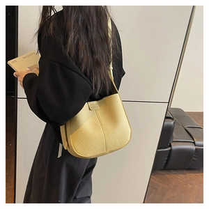 Detail view of a bright yellow litchi grain leather hobo bag worn by a model in a room