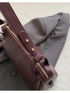 Dettaglio macro della borsa in pelle bordeaux con cerniera dorata e cuciture