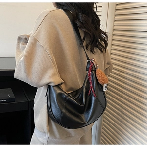 Detail of black leather crescent bag featuring contrast stitching and a plush pompom charm