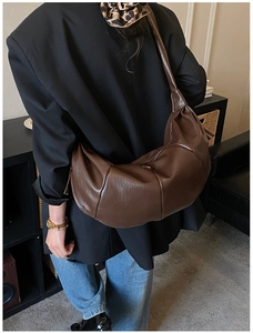 Detail of dark brown croissant bag with pleats shown on shoulder for size reference