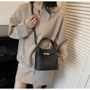 Detail of black lychee grain bucket bag with metal twist lock shown on a model