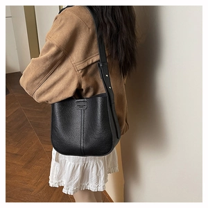 Detail of black pebbled leather bucket bag with wide adjustable strap and metal rivets