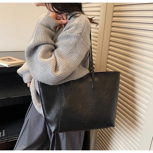 Detail view of a large black vintage tote bag worn by a model in a minimalist home setting