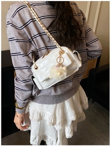 Détail d'un sac bandoulière matelassé blanc avec chaîne en métal et pompon en peluche