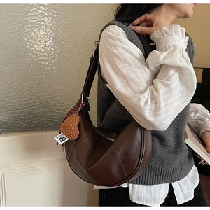 Close-up of dark brown leather hobo bag with plush heart charm and adjustable strap