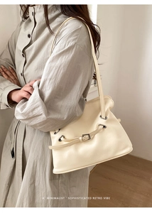Gros plan d'un sac à bandoulière plissé crème avec boucle de ceinture et œillets argentés
