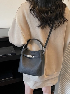 Elegant black lychee leather bucket bag with metal lock shown in a lifestyle street shot
