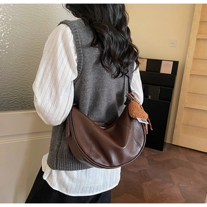 Detail of dark brown crescent bag with smooth faux leather texture and plush charm