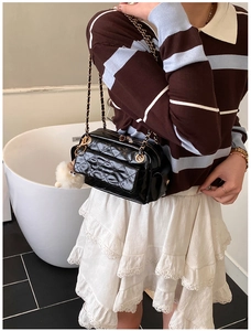 Détail du sac bandoulière noir matelassé avec chaîne et charmant pompon en peluche blanche