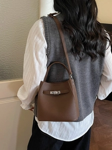 Minimalist dark brown leather bucket bag with metal turn-lock clasp shown on a model