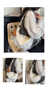 Detail of a creamy white half-moon shoulder bag featuring a brown plush heart charm and zipper