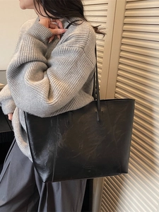 Large black vintage tote bag with thin leather straps shown on a model in a side view
