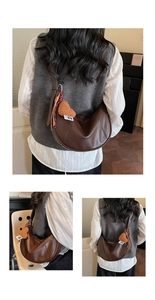 Detail view of dark brown crescent saddle bag with heart-shaped plush charm and zipper