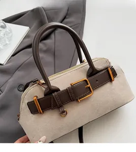 Detail van beige suède handtas met bruine leren riemen en goudkleurige metalen gespen