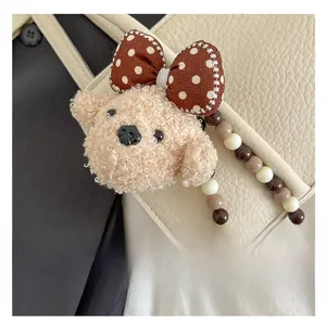 Detail of plush puppy bag charm with polka dot bow and beaded strap on leather bag