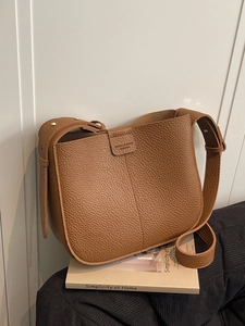 Brown lychee leather crossbody bag on a book showing its texture and golden studs