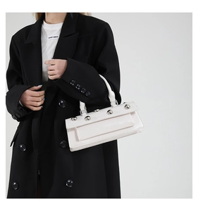 Détail d'un sac à main blanc brillant en cuir verni avec rivets argentés et poignée