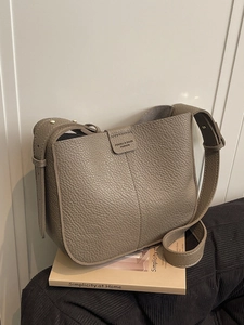 Chic taupe pebbled leather bucket bag with wide strap on a minimalist book setting
