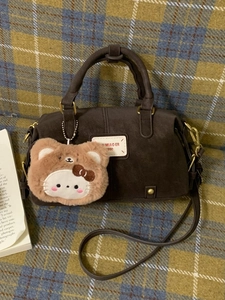 Deep brown minimalist pillow handbag with detachable strap and plush cat charm on plaid cloth