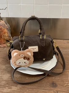 Brown leather Boston bag with plush charm on a wooden table for a vintage look