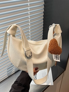 Creamy beige crescent shoulder bag in soft faux leather with brown plush heart pendant