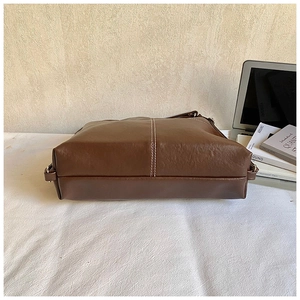 Detailed view of brown leather tote bag showing white contrast stitching and hardware