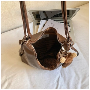 Detail of dark brown tote bag showing striped lining, zipper closure and plush bear charm