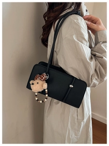 Detail of black rectangular baguette bag with plush bear charm and silver hardware