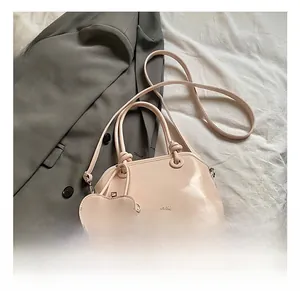 Detail of pink glossy shell handbag with heart charm and brand logo on fabric background