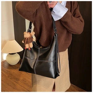 Detail of black PU leather tote with white stitching and a cute bear bag charm