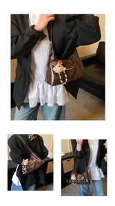Detail of dark brown leather underarm bag with gold metal trim and teddy bear charm
