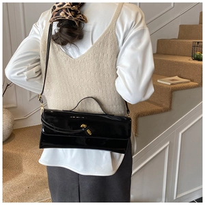 Gros plan du sac à main en cuir verni noir avec fermoir doré porté à l'épaule