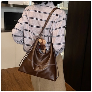 Detail of glossy brown leather tote bag with white stitching and bear charm