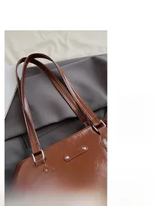 Close-up of polished brown patent leather tote bag straps with silver metal buckles