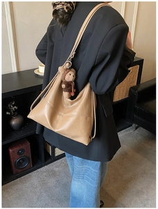 Close-up of camel PU leather tote bag worn on shoulder with a cute brown plush bear charm
